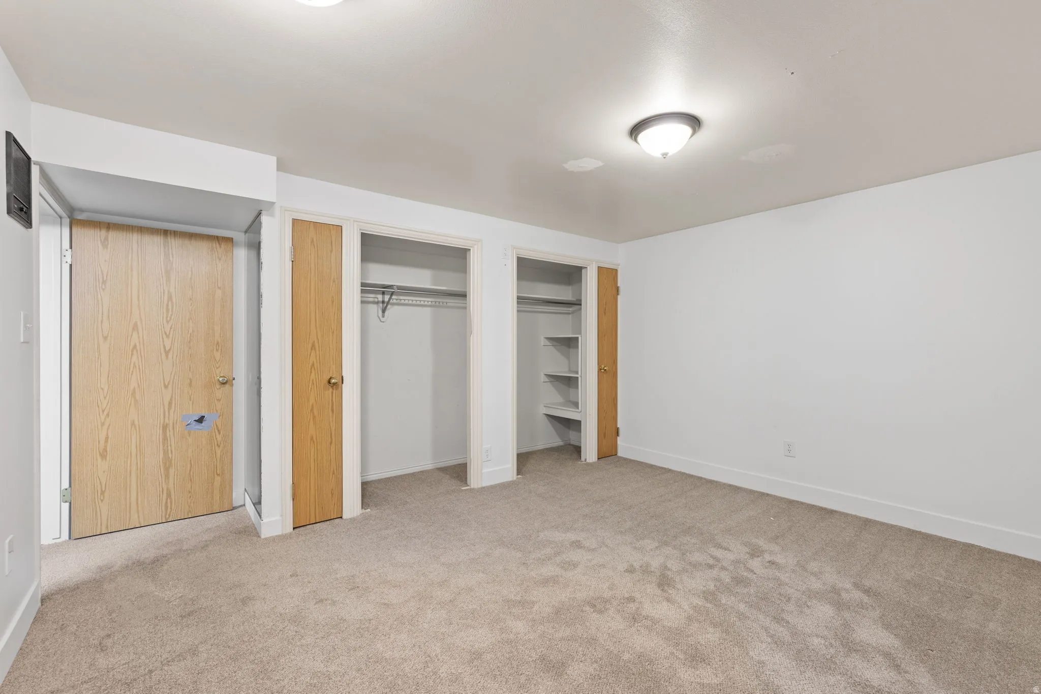 Neutral tone carpeting, white walls, flush mount ceiling lighting, and multiple closet storage options