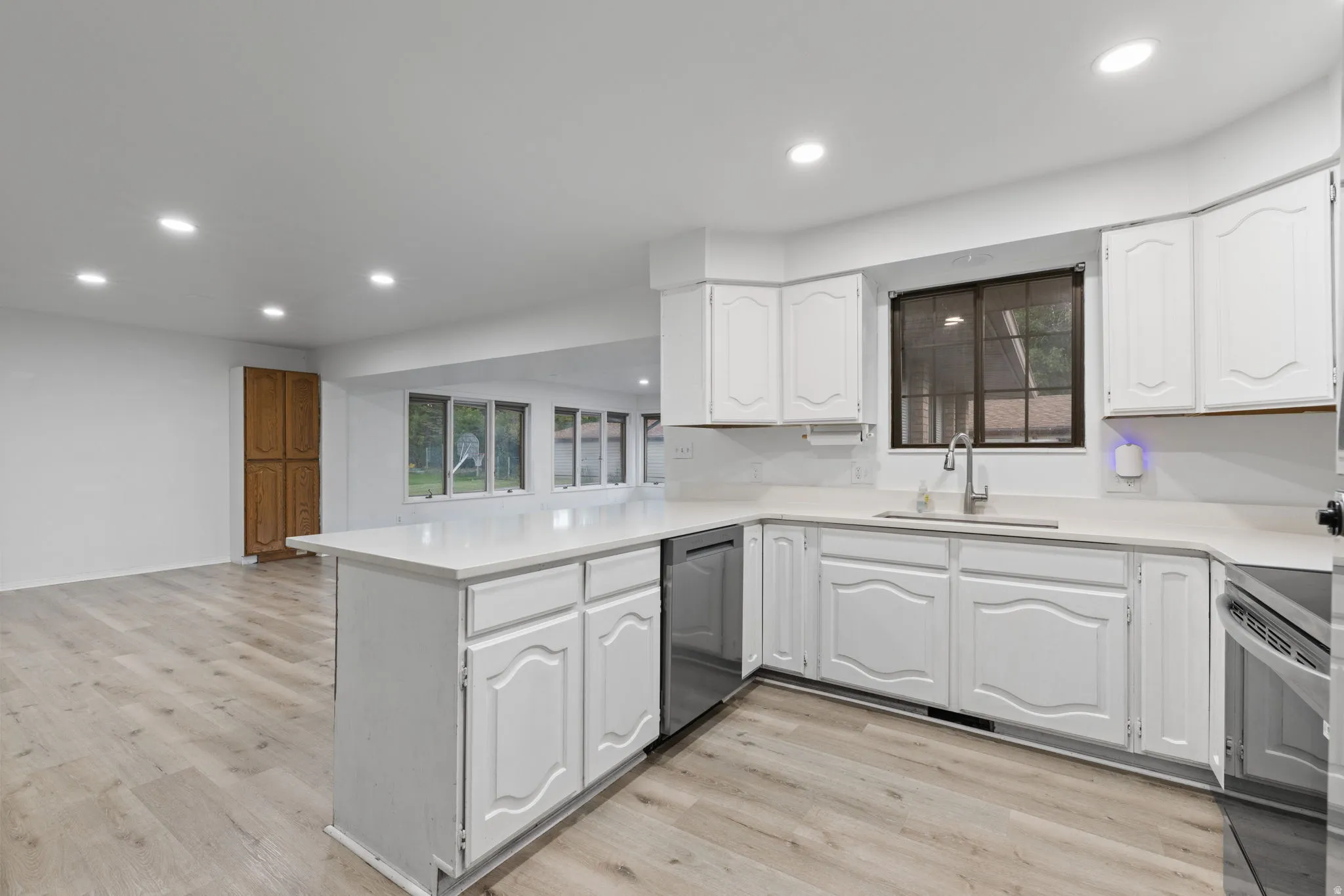 White cabinetry with integrated appliances, light-toned countertops, and wood-finish flooring