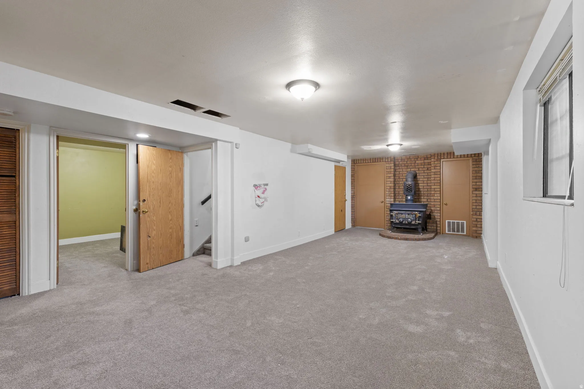 Spacious basement recreation area featuring neutral carpet flooring, recessed ceiling lighting, and multiple wood-finish doors providing flexible room division