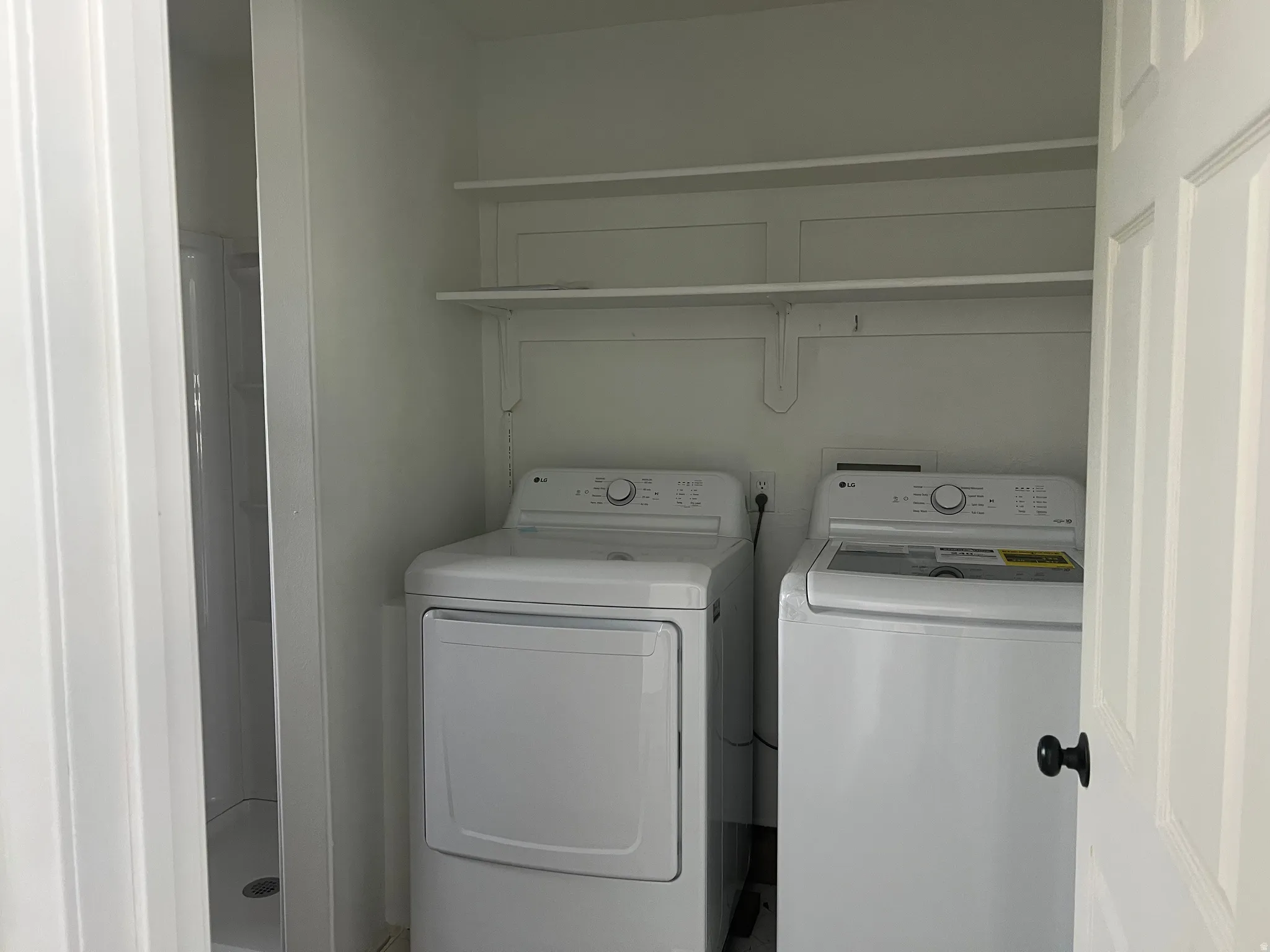 Built-in shelving, white washer and dryer, white paneled door, black door hardware, and white shower stall