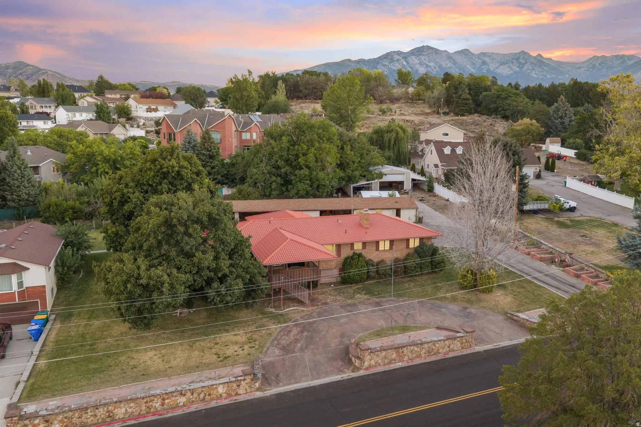 Property featuring a red-toned roof, an expansive paved driveway, and mature landscaping