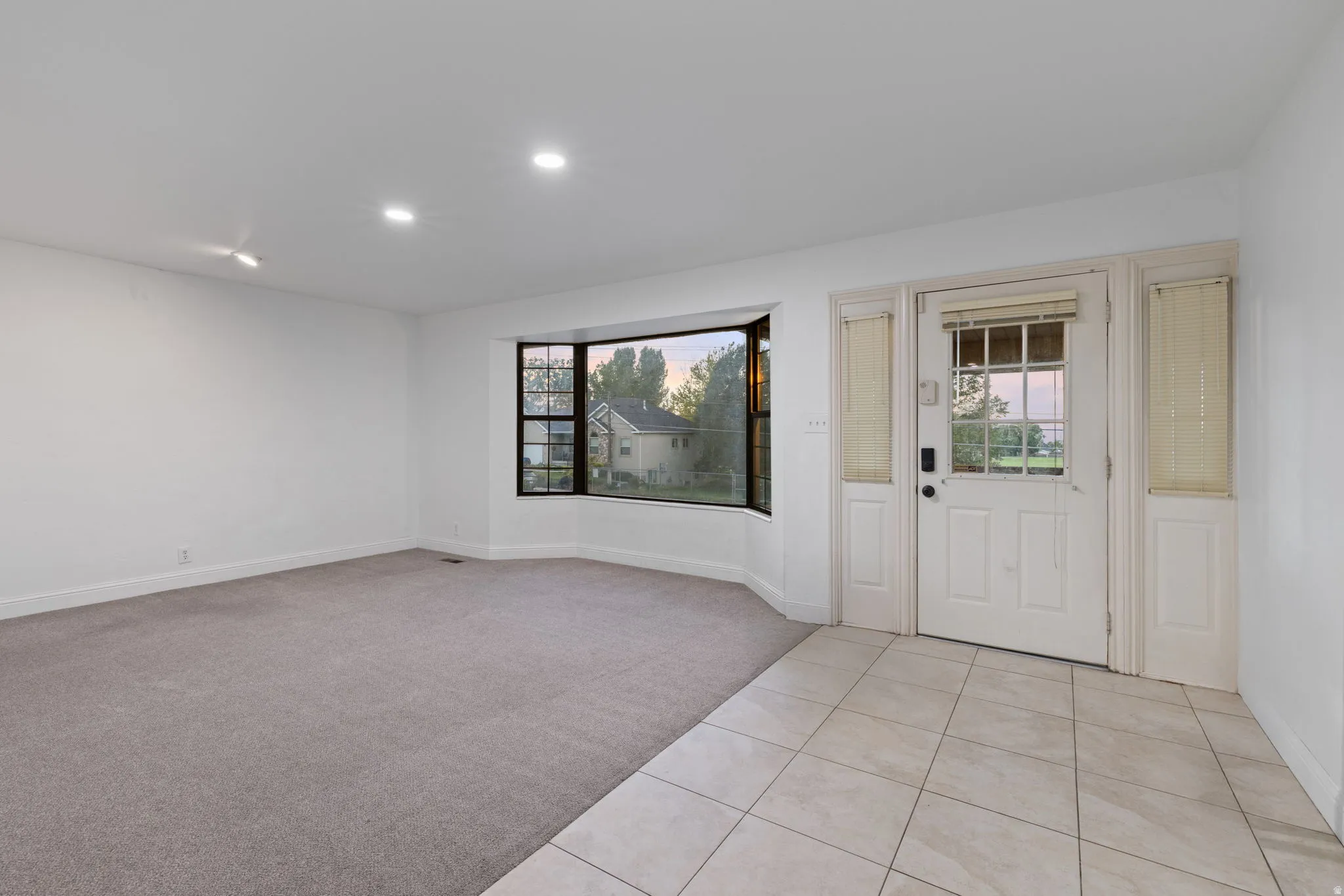 Recessed lighting, bay window, light neutral carpet, tile flooring, and panel door with sidelights