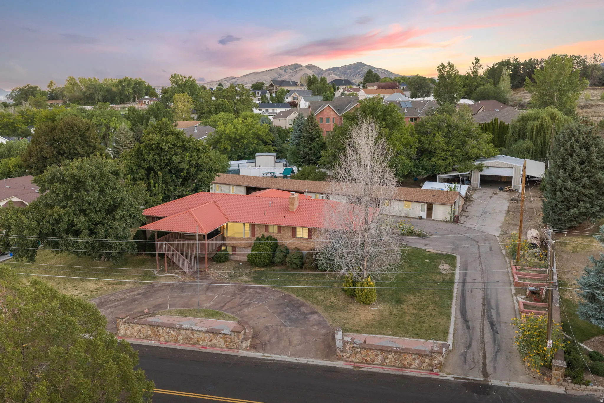 Mountain backdrop, red roof, stone-faced retaining wall, covered porch, multiple outbuildings