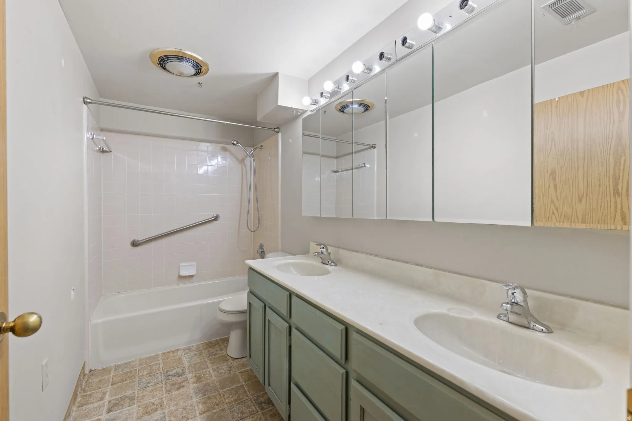 Dual vanity with undermount sinks and chrome fixtures, ample mirrored storage, and a shower-over-tub combination with grab bar