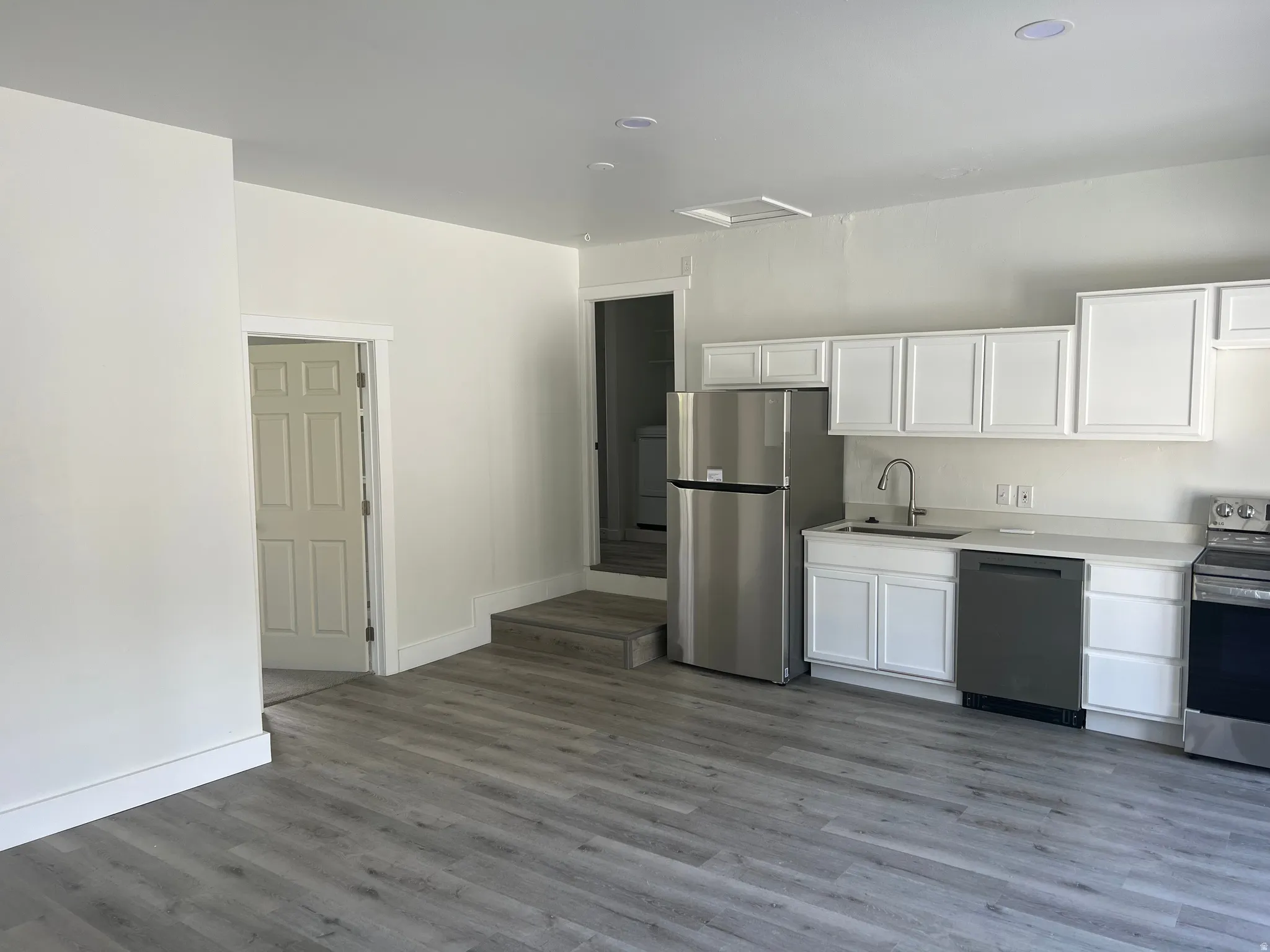 Contemporary kitchen featuring white cabinetry, stainless steel appliances, a stainless steel sink, and light-toned countertops