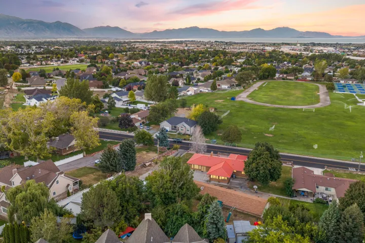 Expansive suburban landscape featuring a prominent red-roofed structure, surrounded by mature trees, a green athletic field, and distant mountains
