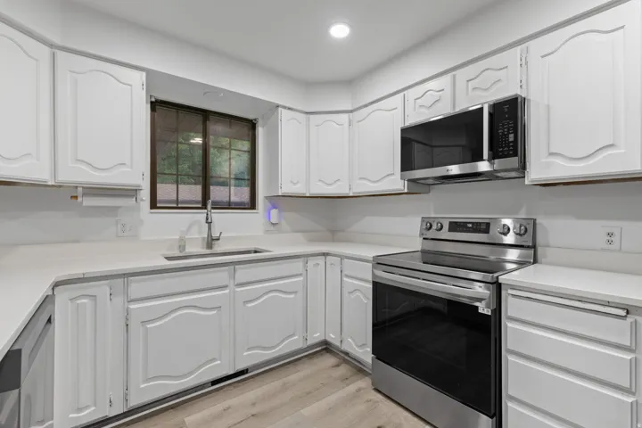 White cabinetry with decorative paneling, light countertops, stainless steel appliances, and wood-finish flooring