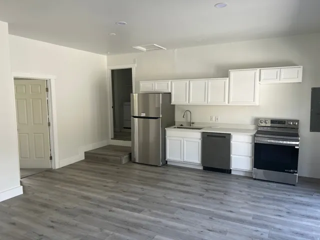 Kitchenette featuring white cabinetry, stainless steel appliances, light-toned countertops, and wood-finish flooring