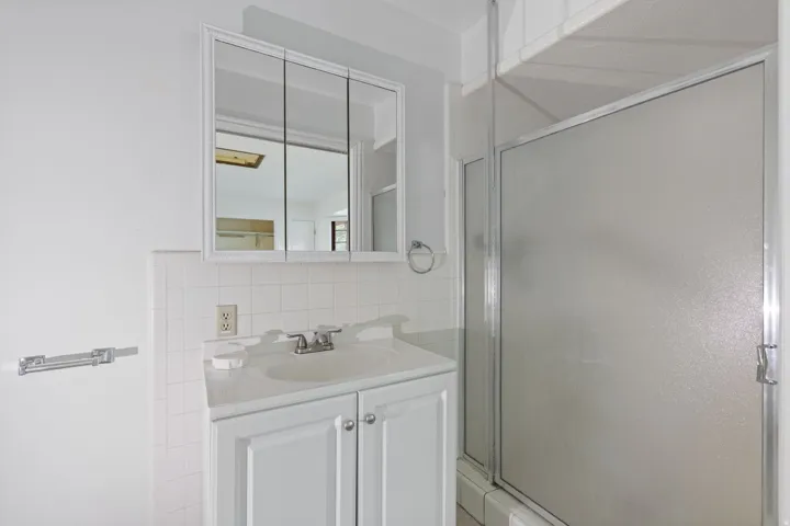 White vanity with integrated sink, chrome faucet, medicine cabinet with mirrored doors, and white subway tile backsplash