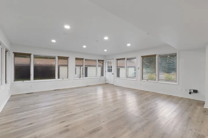Recessed lighting, wood-finish flooring, white walls, multiple windows with blinds, and a white paneled door