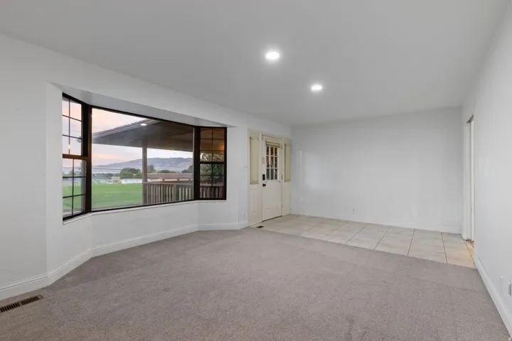 Large bay window, recessed lighting, neutral carpet, tiled entry, and a white paneled door
