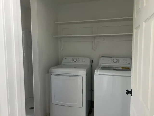 Built-in shelving, white washer and dryer, white paneled door, black door hardware, and white shower stall