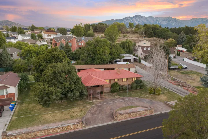 Property featuring a red-toned roof, an expansive paved driveway, and mature landscaping