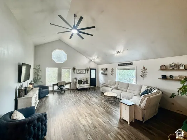 Vaulted ceiling with a large ceiling fan, wood-finish flooring, and multiple windows including an octagonal window