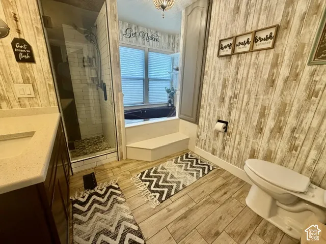 Glass-enclosed shower with subway tile surround and stone floor, wood-finish flooring, built-in bathtub with tiled steps, vanity with integrated sink and light-toned countertop, and wood-paneled walls