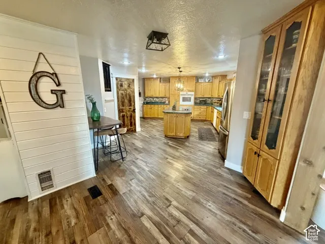 Wood-finish flooring throughout, complemented by a kitchen featuring wood cabinetry, a central island, and stainless steel appliances