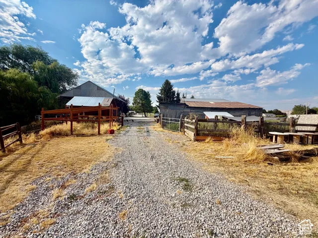 Gravel driveway leading to a barn with a metal roof and a wooden fence, accompanied by a second outbuilding featuring a metal roof