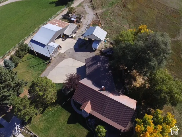 Property featuring a metal roof structure, additional outbuildings, paved and unpaved driveways, and mature trees