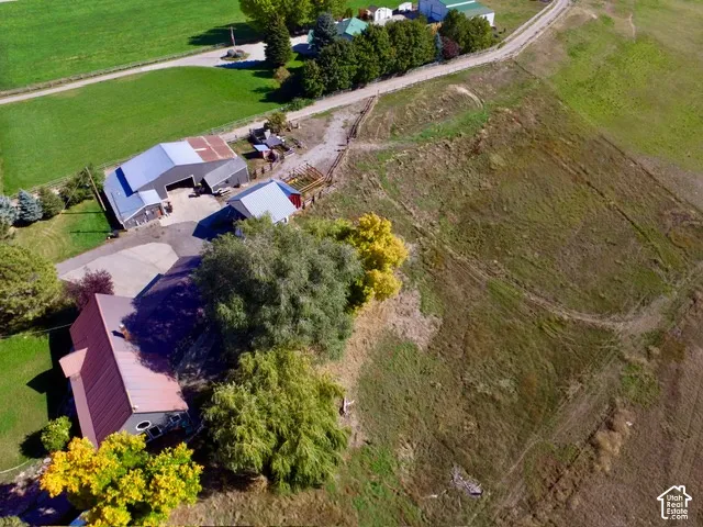 Aerial view showcasing a productive agricultural property with modern farm structures, mature landscaping including established trees, manicured lawn areas, and expansive cultivated fields
