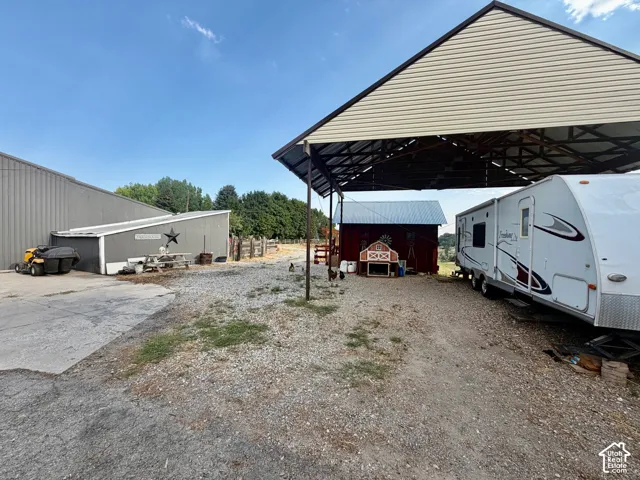 Gravel parking area featuring a large metal-framed carport, red barn, and a gray-sided outbuilding