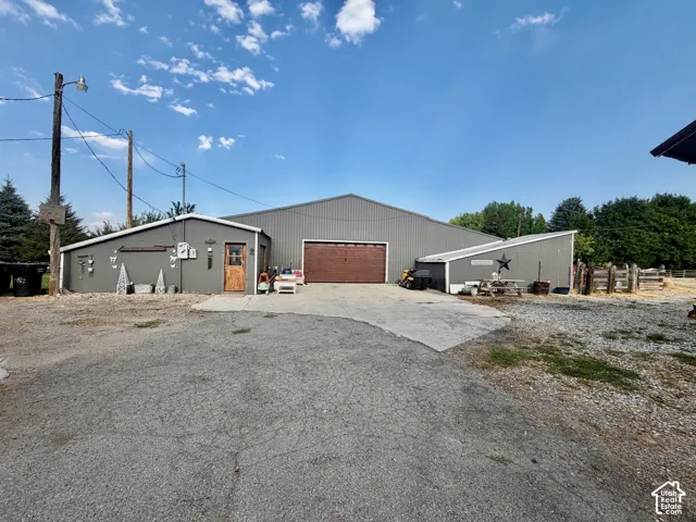 Metal-sided barn structure with a large roll-up door, accompanied by two additional sloped-roof outbuildings