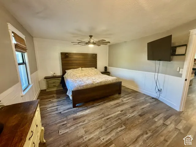 Wood-finish flooring, paneled wall detailing, built-in ceiling fan, and window with a shade