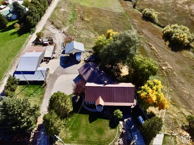 Expansive property featuring a residence with a rust-colored metal roof, multiple outbuildings with gray metal roofs, a paved driveway, and established landscaping with mature trees