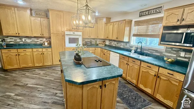 Kitchen featuring a central island with cooktop, wood-finish flooring, light wood cabinetry, a built-in oven, and a double basin sink
