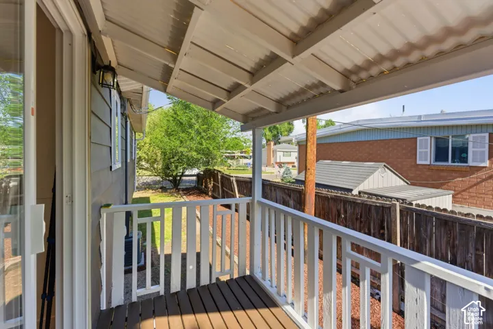 Covered outdoor deck with wood-finish flooring, white railing, and a corrugated metal roof