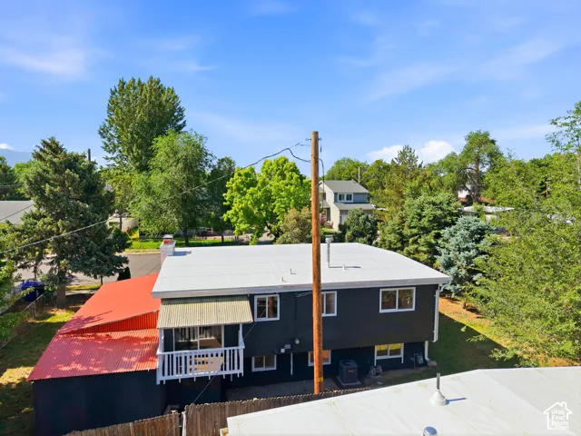 Exterior featuring dark siding, white trim windows, white balcony railing, a white balcony awning, and a red corrugated metal roof extension