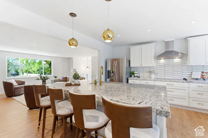 Kitchen island with granite countertop, wood-finish flooring, white cabinetry, stainless steel appliances, and a unique tiled backsplash