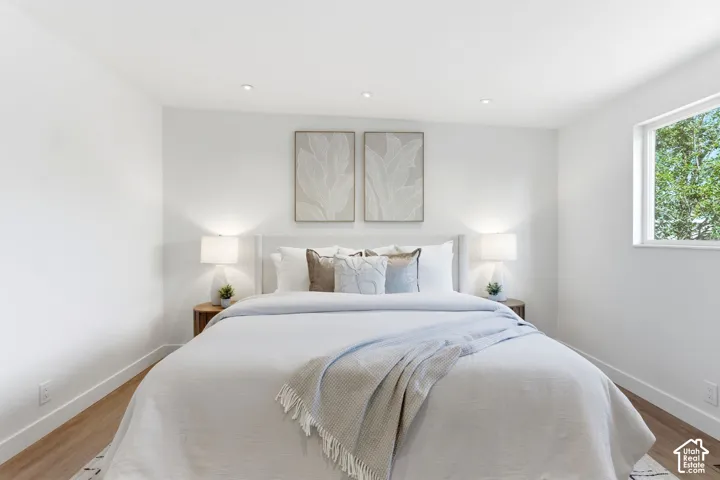 Recessed ceiling lighting, a framed window, light wood-finish flooring, and a white upholstered headboard