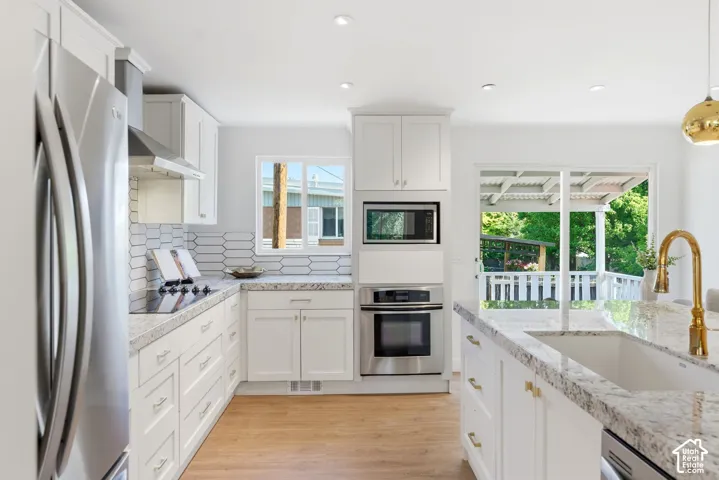 Kitchen featuring white cabinetry, light-toned wood-finish flooring, stainless steel appliances, granite countertops, and an undermount sink with a gold-finish faucet