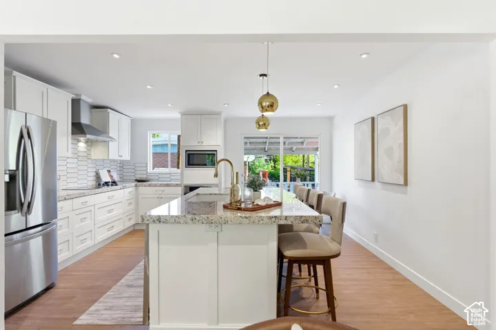 Modern kitchen featuring white cabinetry, stainless steel appliances, a center island with bar seating, and wood-finish flooring