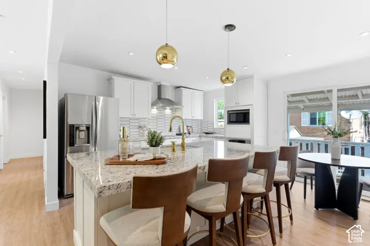 Kitchen featuring a large island with stone countertop, stainless steel appliances, white cabinetry, and wood-finish flooring