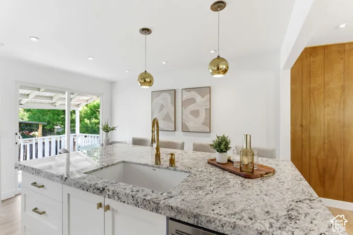 Kitchen island with a built-in sink, granite countertop, white cabinetry, and gold-tone hardware