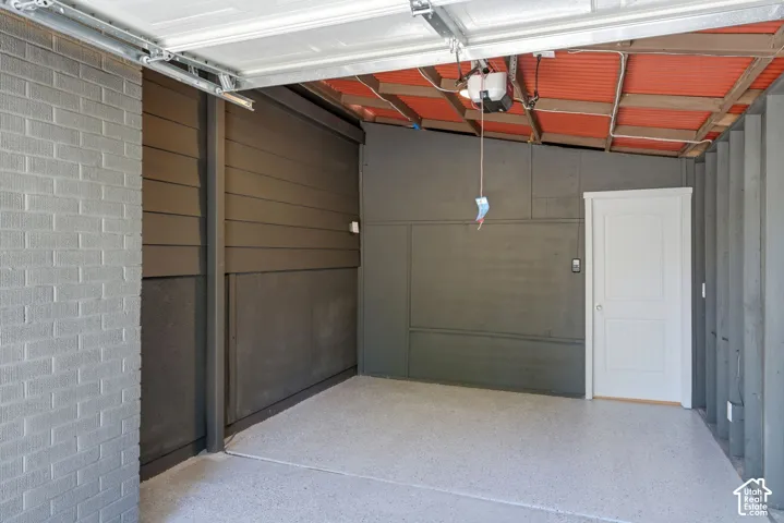 Garage with a light gray epoxy floor finish, gray brick wall, and a white access door