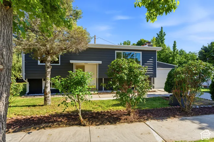 Contemporary exterior siding, attached garage, concrete driveway, front lawn, and mature landscaping