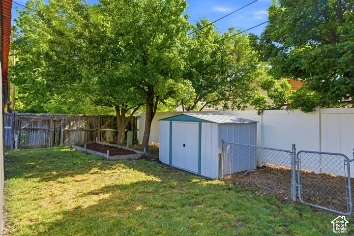 Spacious backyard retreat featuring mature shade trees, a level lawn, storage shed with blue and white finish, and secure chain-link fencing