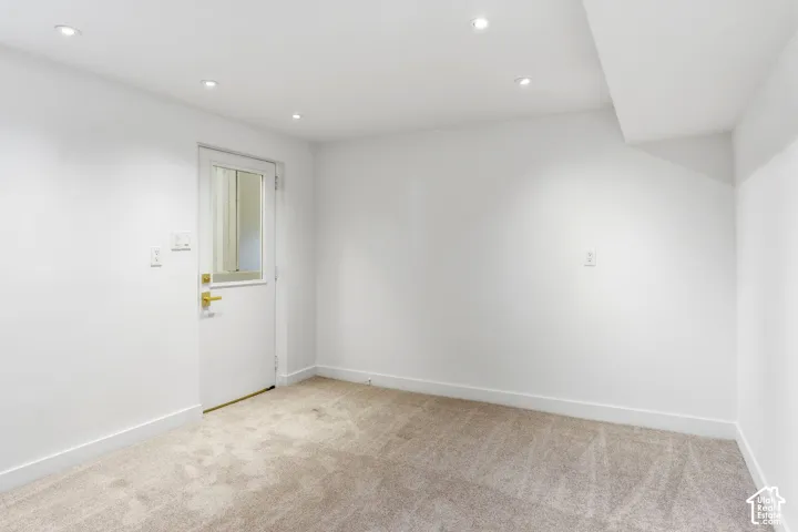 Recessed ceiling lighting, white painted walls, light-toned carpeting, white trim, and a door with a glass panel