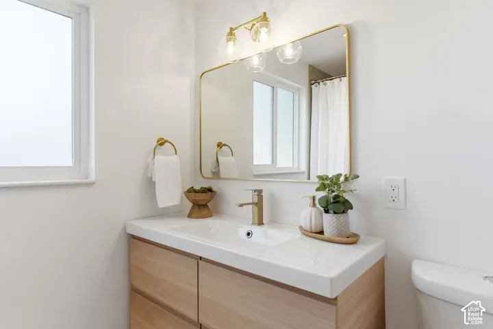 Wood-finish vanity with integrated sink, gold-finish faucet, and coordinating mirror with overhead lighting