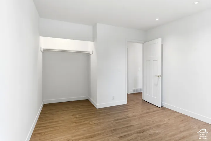 Recessed lighting, wood-finish flooring, white walls, and a built-in closet rod