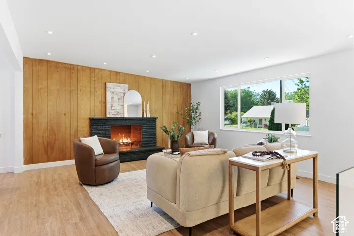 Wood-finish flooring throughout, featuring recessed ceiling lighting, a prominent stone fireplace, and a large picture window