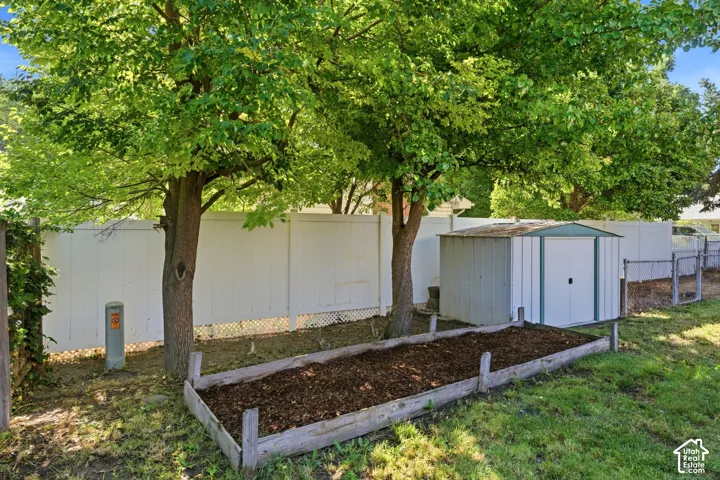 Mature trees, white privacy fencing, raised garden bed, metal storage shed, and chain link fence