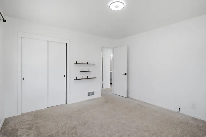 Wall-to-wall carpeting, sliding closet doors, wall-mounted shelving, and a flush-mount ceiling light