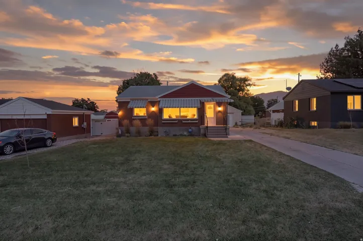 Brick exterior with contrasting striped awnings, manicured front lawn, and concrete driveway leading to a detached garage