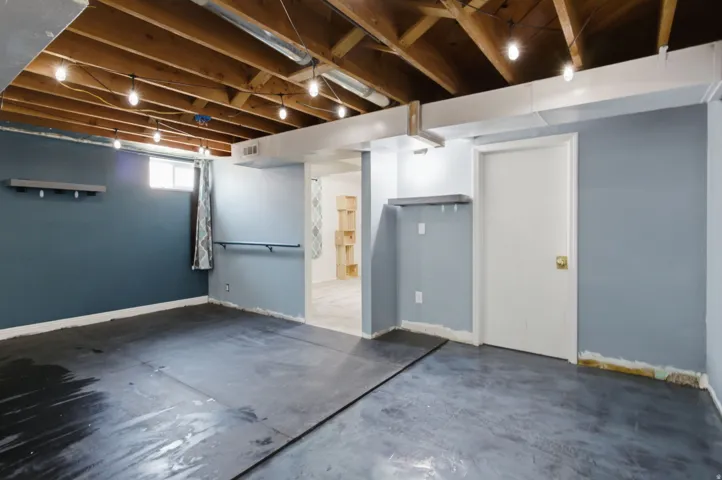 Finished basement featuring exposed wood-beam ceiling with recessed lighting, concrete flooring, blue-painted walls, and separate utility room with refrigerator and water heater