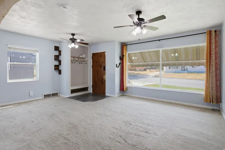 Expansive front window, wood-finish entry door, built-in shelving, two ceiling fans, and entry area with built-in storage