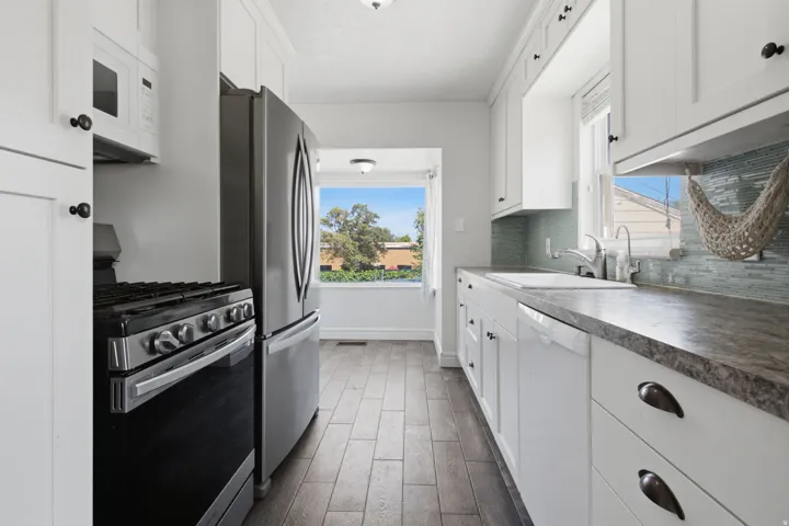 Kitchen featuring white shaker-style cabinetry, wood-finish flooring, stainless steel appliances, and a tile backsplash