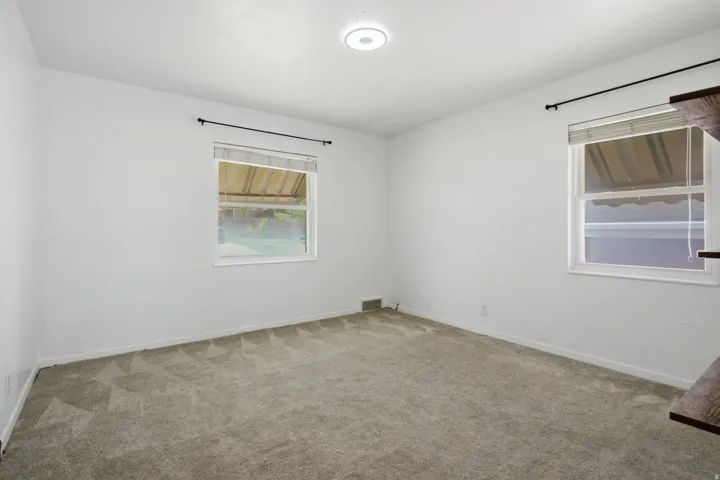 Bright secondary bedroom featuring neutral carpeting, dual windows with natural light, recessed ceiling lighting, and clean white walls throughout